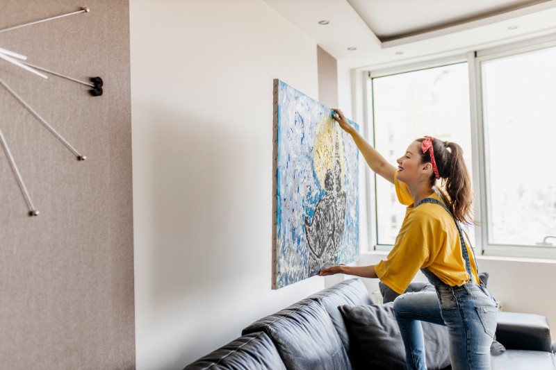 Young woman hanging art picture on wall